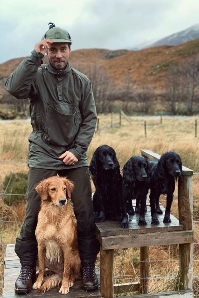 Foto colorida de homem branco, barbudo, ajoelhado. Ele está rodeado de cães com o pelo na cor preta e caramelo - Metrópoles