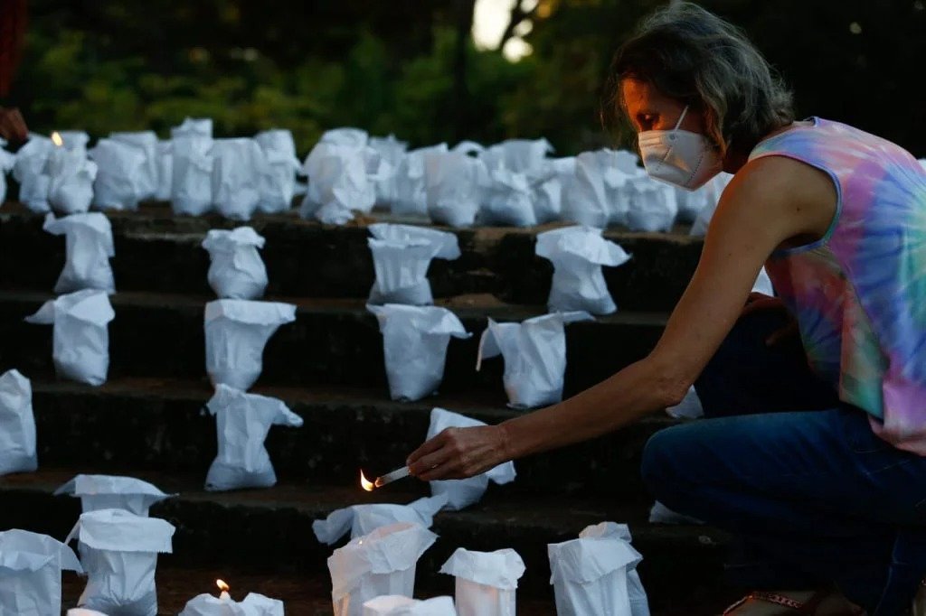 Imagem mostra pessoa acendendo velas em homenagem às vítimas de covid