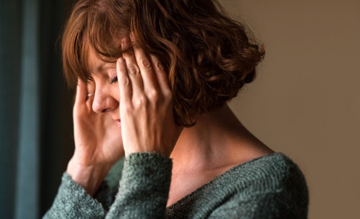Imagem colorida de mulher de perfil com mãos na cabeça ilustra sintomas da menopausa - Metrópoles