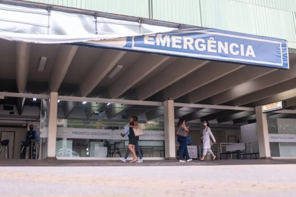 Fachada do Hospital de Base do Distrito Federal, com banner escrito "Emergência" caindo pela metade