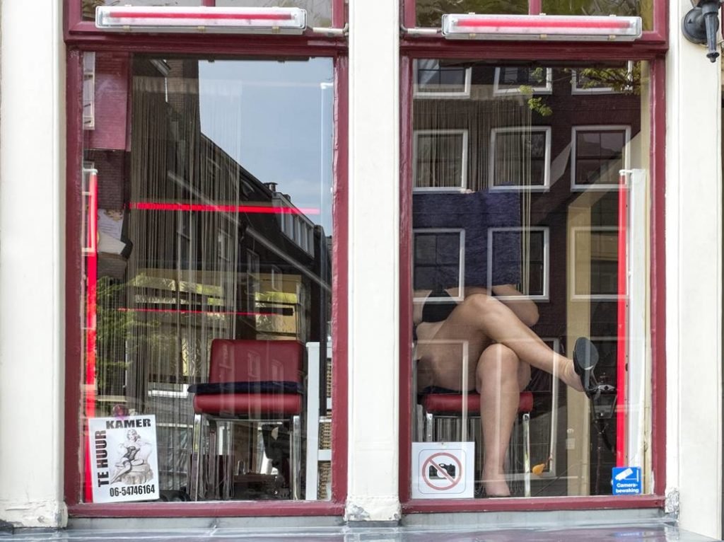 Foto de um prostíbulo em Amsterdã mostrando duas vitrines em que uma delas aparece uma garota de programa seminua e tampando o rosto com um pano