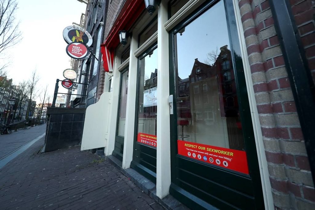 Foto de uma das ruas do Red Light District, em Amsterdã, que mostra a vitrine de um prostíbulo com a mensagem
