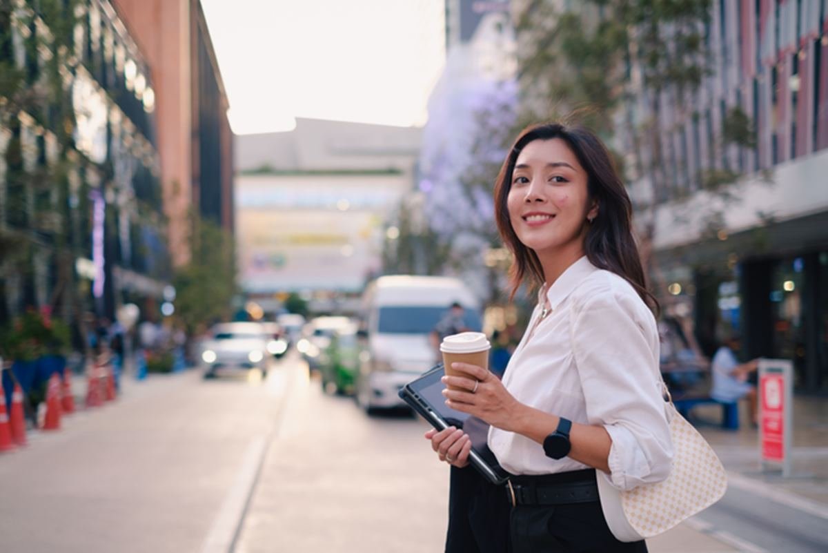 Imagem colorida: mulher na rua com copo de café e tablet - Metrópoles