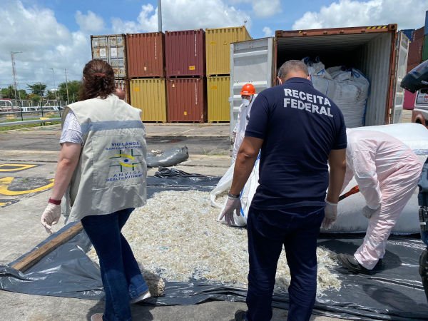 homens com uniforme onde se lê receita federal inspecionam objetos no chão