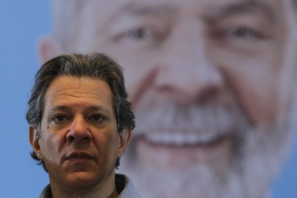 Imagem colorida mostra Fernando Haddad diante de imagem de Lula - Metrópoles