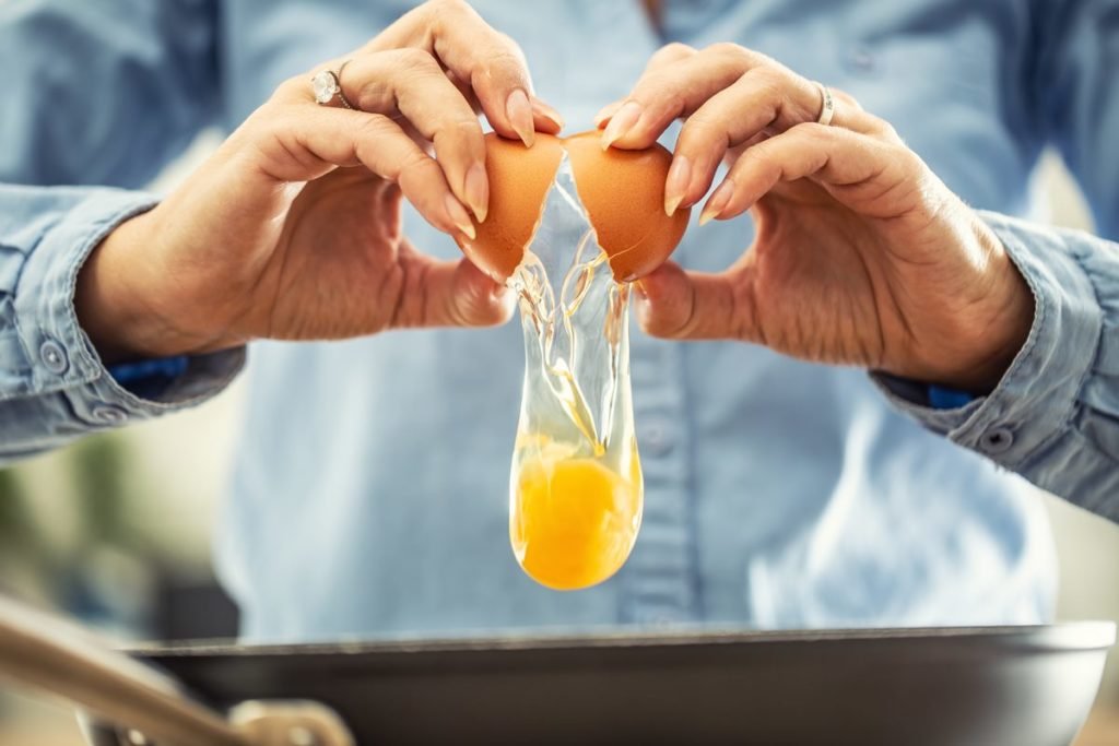 Fotografia de mulher quebrando um ovo na panela - Metrópoles
