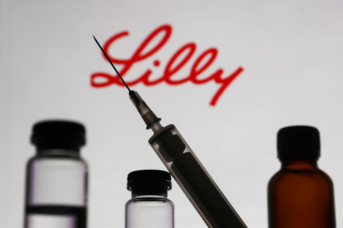 Fotografia de frascos de remédio e seringa com o símbolo da farmacêutica Eli Lilly ao fundo - Metrópoles