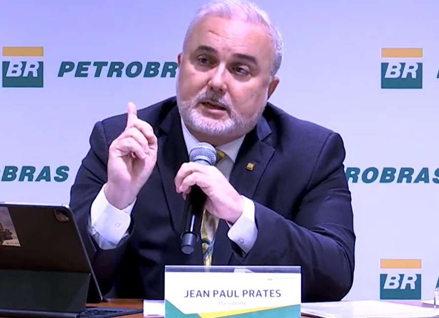 Imagem colorida de Jean Paul Prates, sentado em uma mesa e de terno, em parede com logotipo da Petrobras - Metrópoles