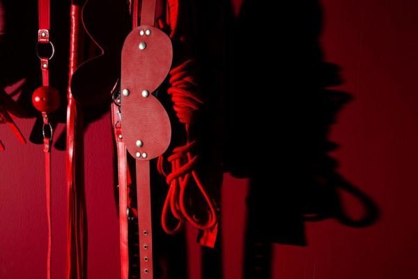 Itens BDSM dispostos em uma parede vermelha - Metrópoles
