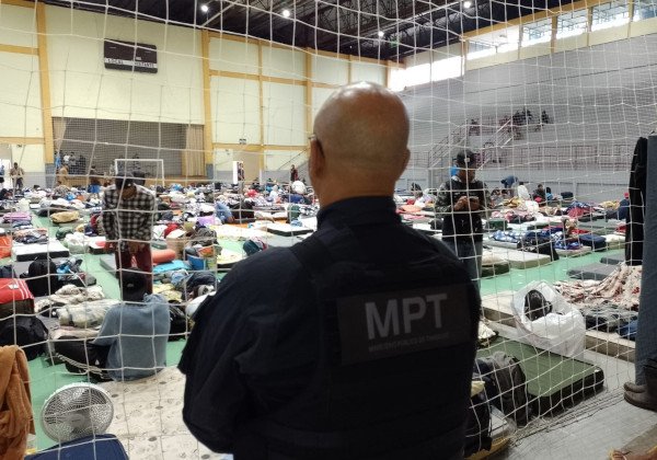 homem com uniforme do MPT de costas olha pessoas em um ginásio