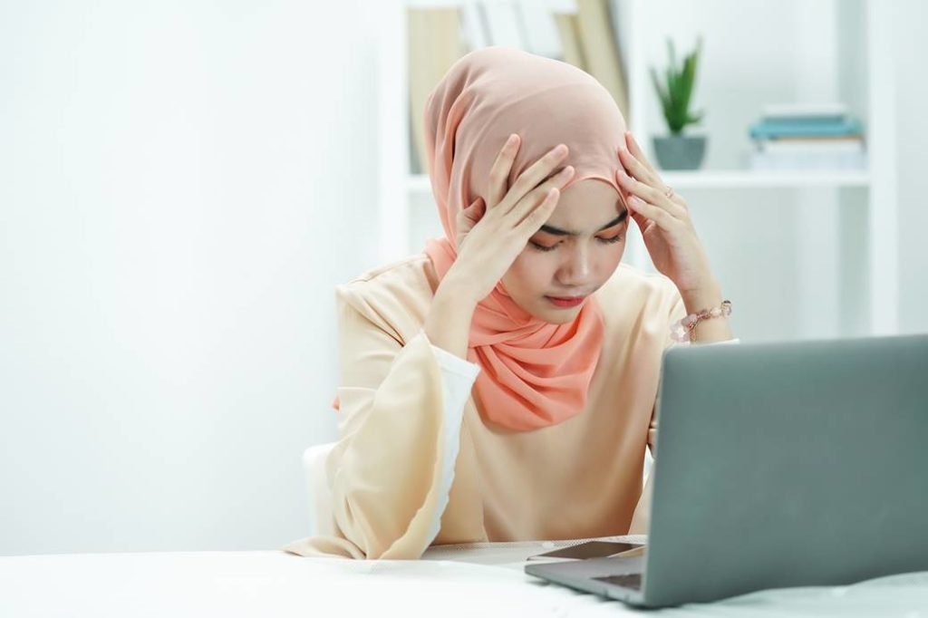 Mulher mulçumana com cara de preocupada em frente ao computador