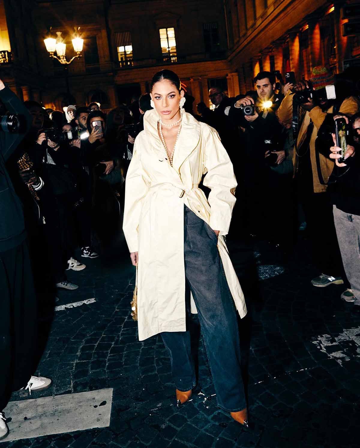 A modelo e ex-BBB Mari Gonzalez no desfile da marca Isabel Marant na Semana de Moda de Paris. Ela é uma mulher branca e jovem, de cabelo liso castanho, e usa uma calça jeans larga e um casaco sobretudo branco, além de brincos e colares de pérolas. - Metrópoles