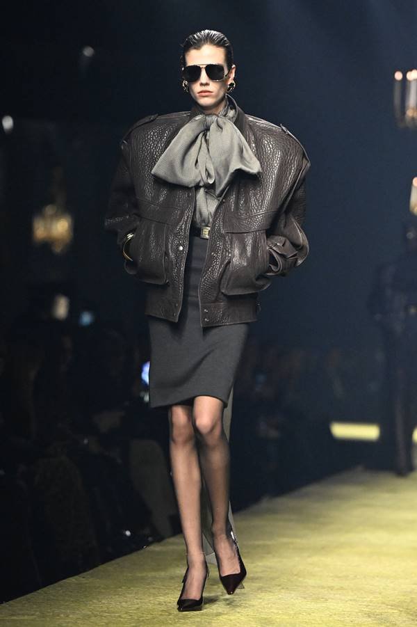 Modelo usa saia lápis preta, casaco de couro preto e blusa de gola com laço grande - Metrópoles 