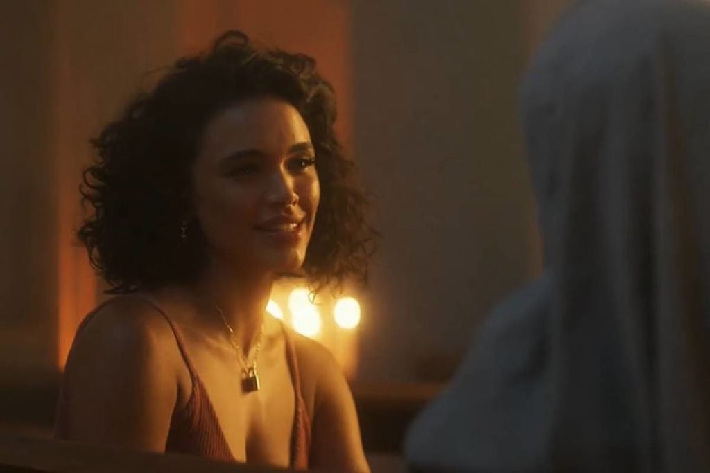 mulher de cabelos cacheados olha sorrindo - metrópoles