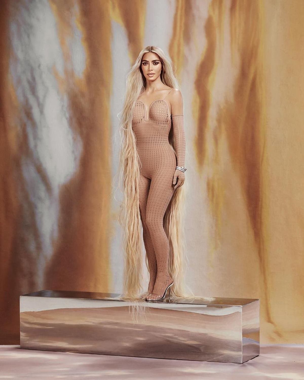 A empresária Kim Kardashian em ensaio fotográfico para a revista Allure. Ela é uma mulher branca e de meia idade, com o cabelo liso e loiro, e usa um macacão bege com uma sandália de salto da marca Paris Texas. - Metrópoles