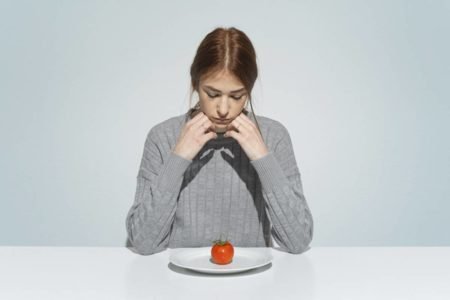 Mulher abaixo do peso olhando chateada para prato com pouca comida