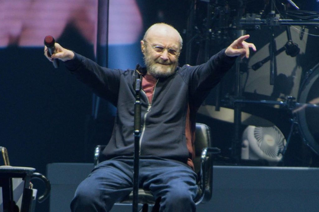 Phil Collins sentado em palco - metrópoles