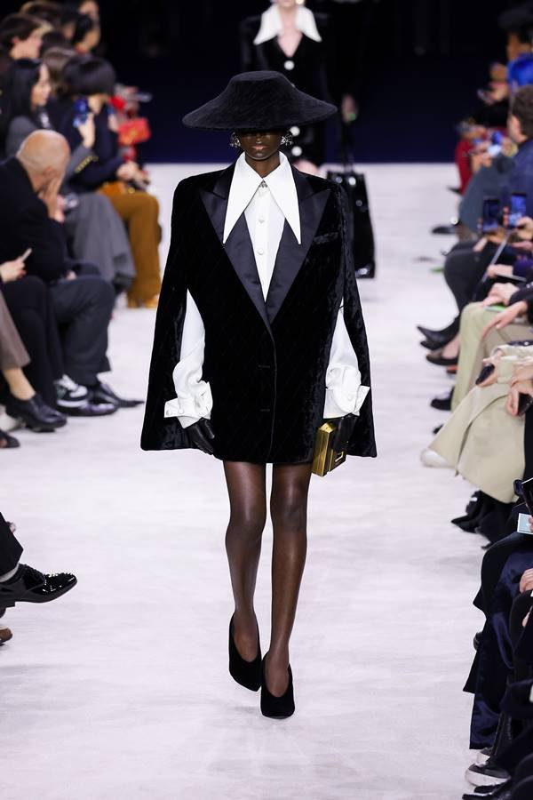 Modelo negra na passarela de moda usa camisa branca com gola pontuda, casaco morcego e saltos altos - Metrópoles 