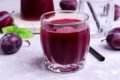 Copo de suco de ameixa com ameixas em volta