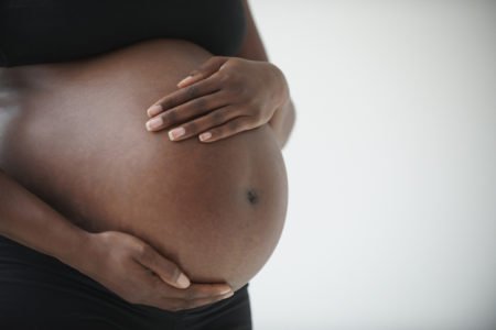 Imagem colorida: mulher negra grávida com mãos na barriga - Metrópoles