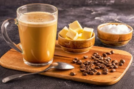 Bulletproof coffee com grãos de café sobre uma tabua com manteiga e colher por cima-Metrópoles