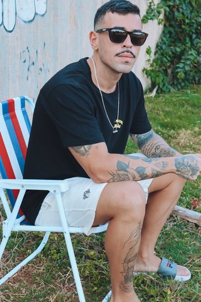 João Pedro De Lamare da marca Tha f*ck sentado em cadeira de praia com peças da etiqueta - Metrópoles