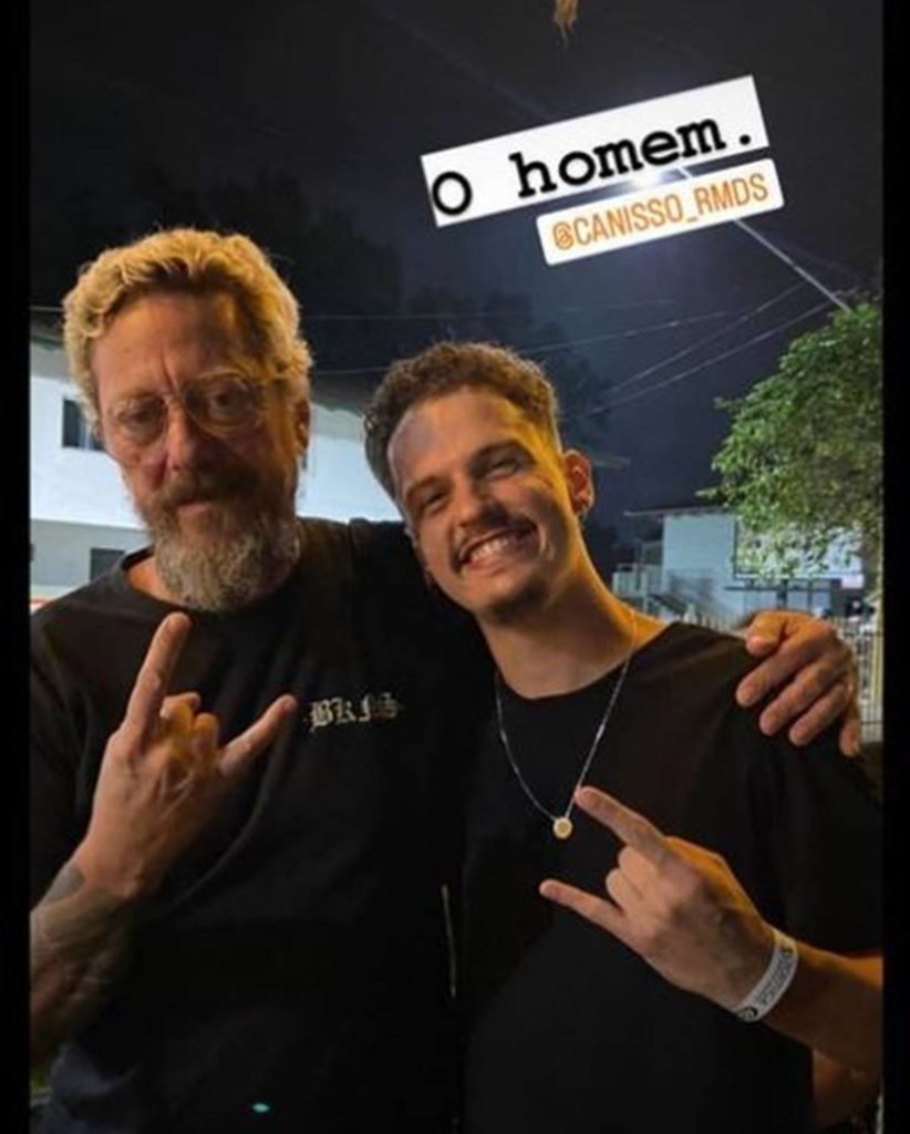 canisso abraçado em fã homem de camiseta preta, os dois fazem sinal de rock com uma mão - metrópoles