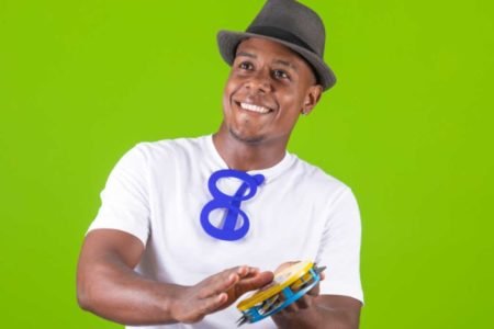 Homem com blusa branca com pandero na mão e fundo verde
