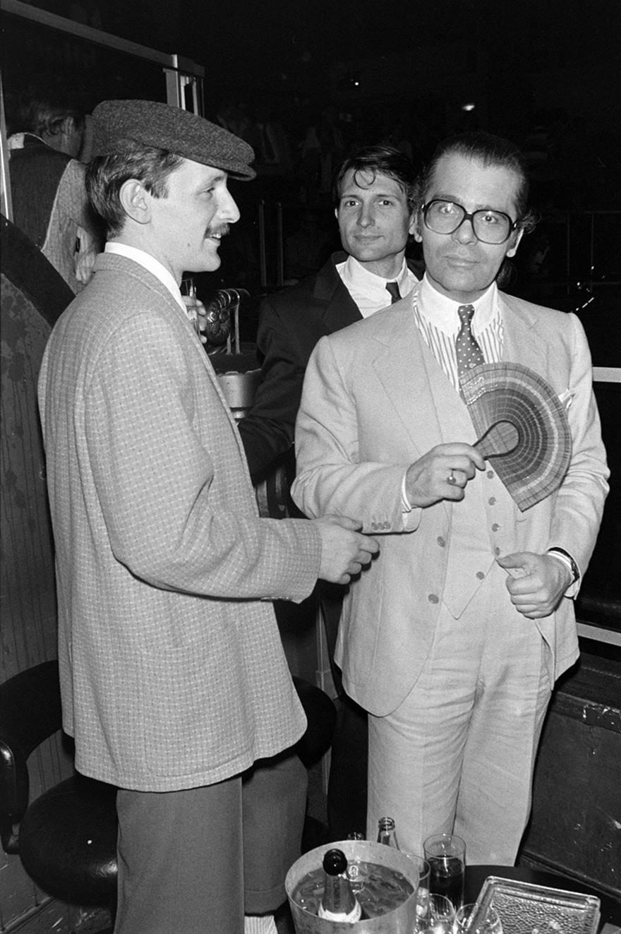 Jacques de Bascher e o estilista Karl Lagerfeld em 1979. A foto é preta e branca. Os dois usam roupas encomadas, como camisas, gravatas e blazers. - Metrópoles