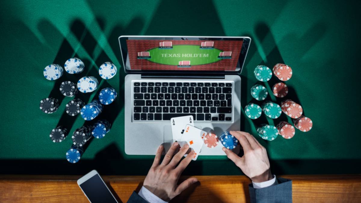 Fotografia colorida mostrando mãos de homem de terno mexendo em cartas de baralho em cima de computador com jogo de cassino na tela-Metrópoles