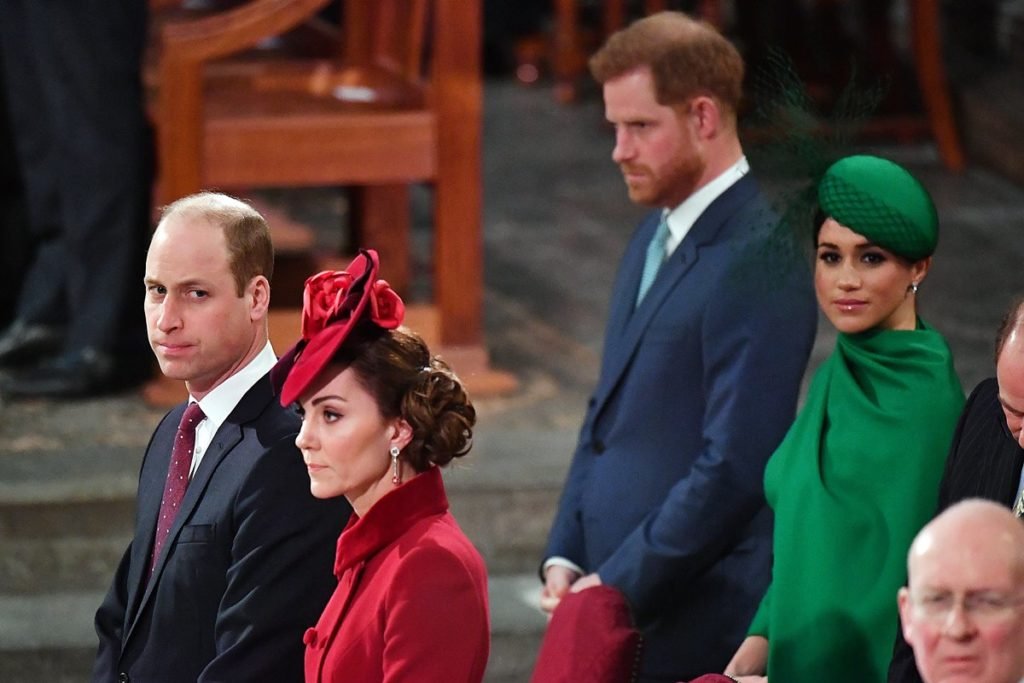 Foto colorida de dois casais, um à frente e outro atrás, os homens usam terno e as mulher vestem roupas monocromáticas, um de vermelho e a outra com roupa verde - Metrópoles