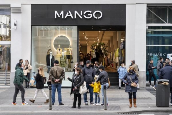 Loja de rua da marca de roupas Mango, na Espanha, na Europa. É possível ver pessoas andando na rua e entrando e saindo do estabelecimento. - Metrópoles