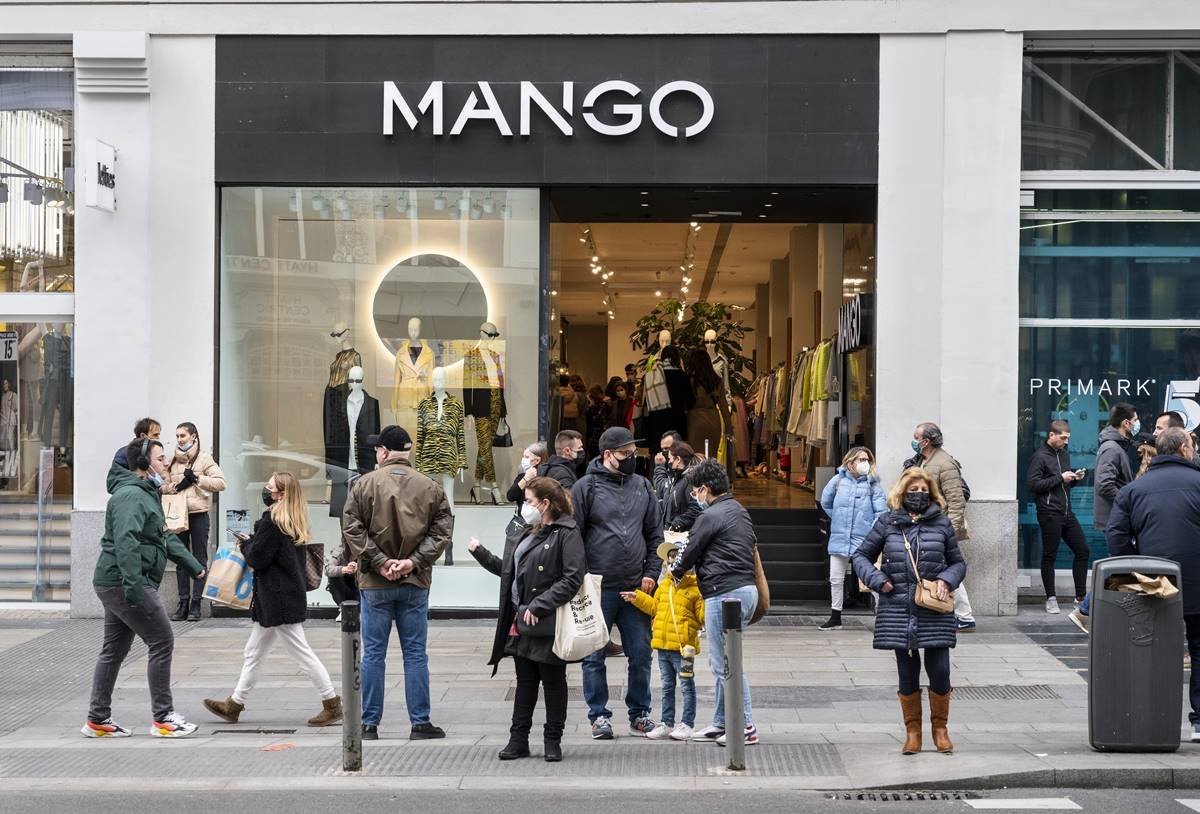 Loja de rua da marca de roupas Mango, na Espanha, na Europa. É possível ver pessoas andando na rua e entrando e saindo do estabelecimento. - Metrópoles