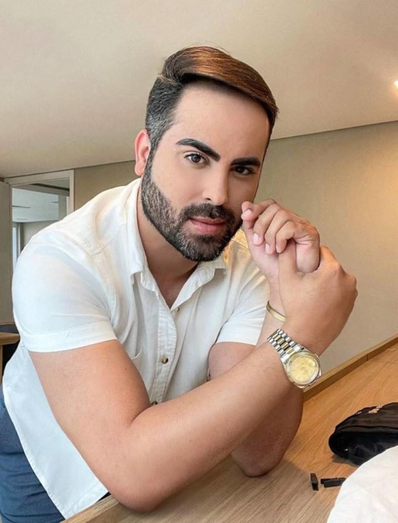 home com barba e polo branca posa sério sobre mesa - metrópoles