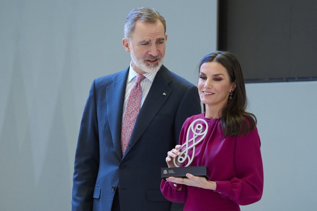 Foto de homem, com blazer preto e gravata rosa. Ele tem cabelo grisalho e está ao lado de mulher, com cabelo de tamanho mediano, com roupa na cor fúcsia. Ela está segurando um prêmio - Metrópoles