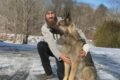 Cachorro pastor alemão com um homem ao lado dele de calça preta e blusa de frio cinza e touca na neve- metrópoles