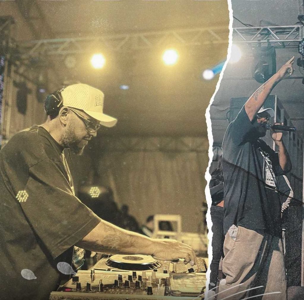 Foto recortada. DJ Jamaika levanta as mãos em uma e mexe em mesa de DJ na outra