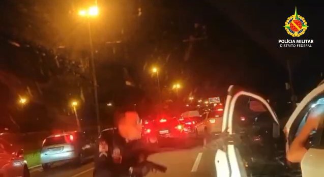 Policial militar fardado abre porta de carro branco e segura pistola