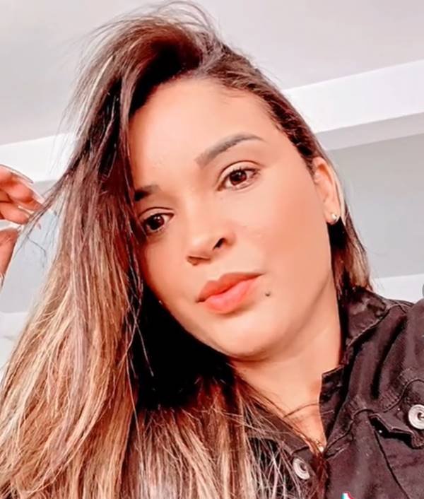 Mulher branca de cabelos morenos e lisos passa mão no cabelo liso