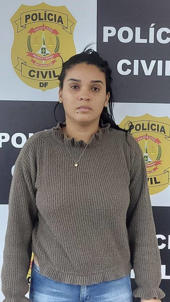 Mulher branca veste casaco marrom e posa para foto na polícia