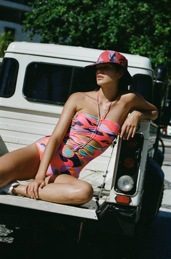 Usando maiô colorido e chapéu, mulher está sentada em traseira de carro - Metrópoles
