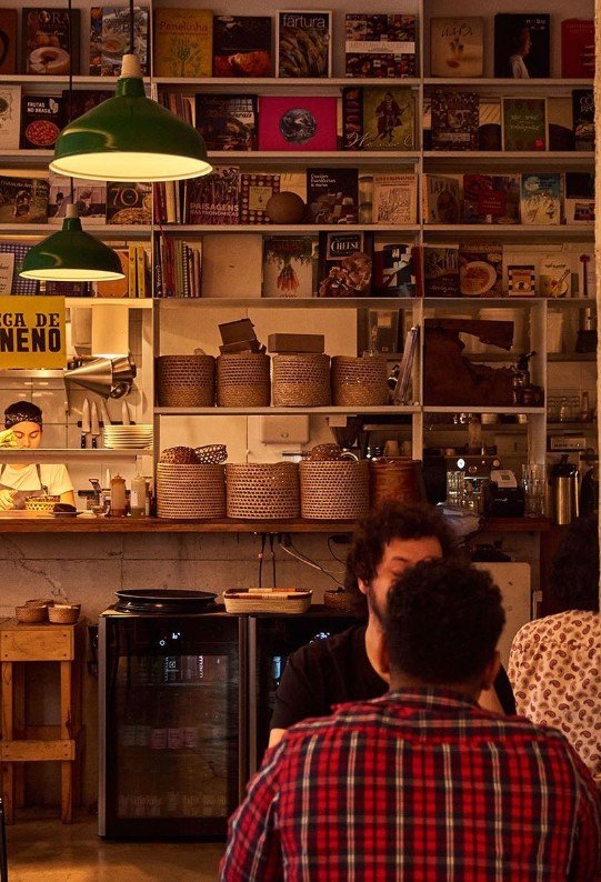 Foto que mostra vários livros e a cozinha do restaurante Cuia - Metrópoles