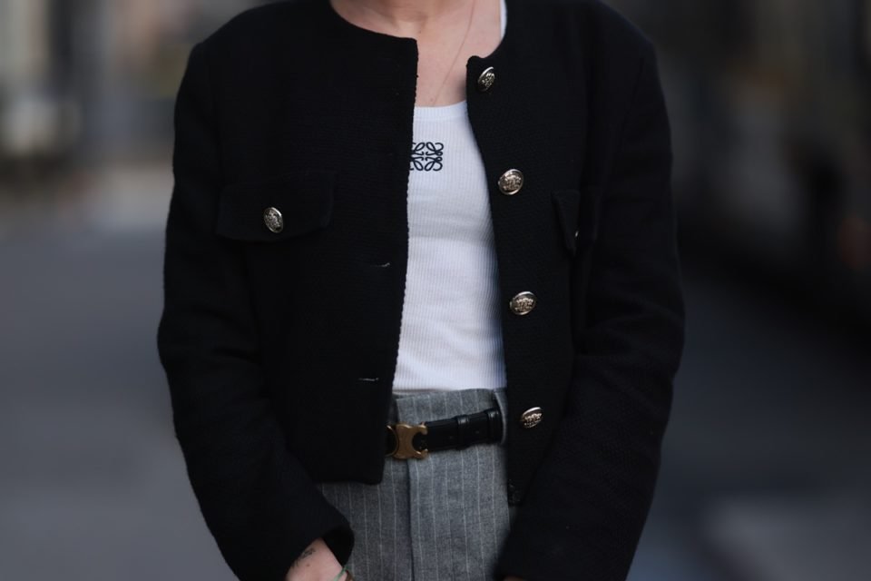 Mulher branca usa look durante a Semana de Moda de Paris. Ela veste uma regata branca com a marca da Loewe, um casaquinho preto e uma calça cinza. - Metrópoles