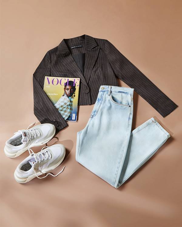 Foto de um blazer curto, acima de uma calça jeans, tênis branco e uma revista Vogue - Metrópoles