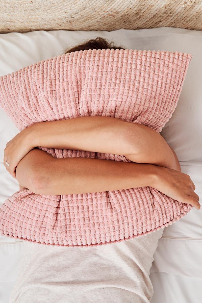 Foto colorida de mulher deitada abraçando travesseiro, com fronha rosé - Metrópoles