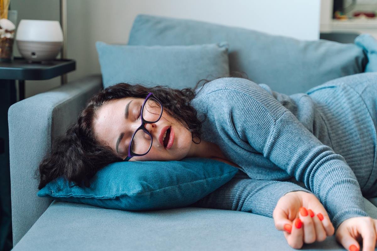 Foto colorida de mulher, branca e de óculos, dormindo em um sofá - Metrópoles