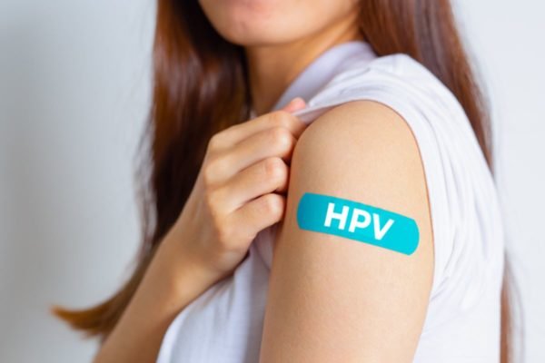 Imagem colorida: mulher de perfil mostra curativo no braço escrito HPV - Metrópoles