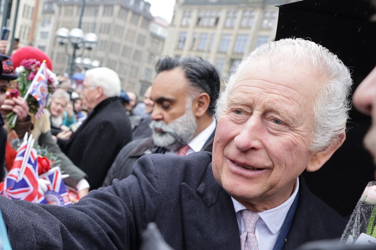 Foto colorida de homem idoso e branco rodeado de pessoas com bandeiras do Reino Unido - Metrópoles