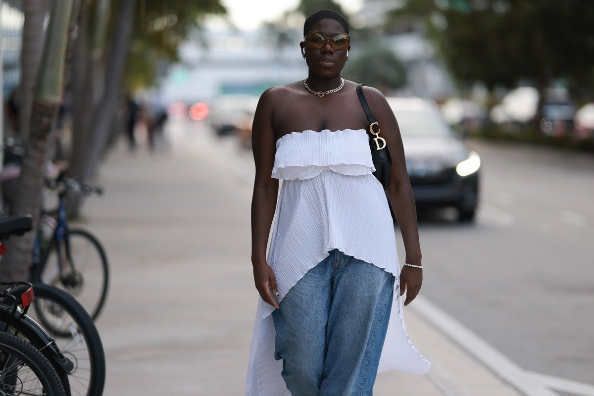 Mulher careca usa look com blusa branca sem alças com calça jeans e bolsa baguete preta - Metrópoles