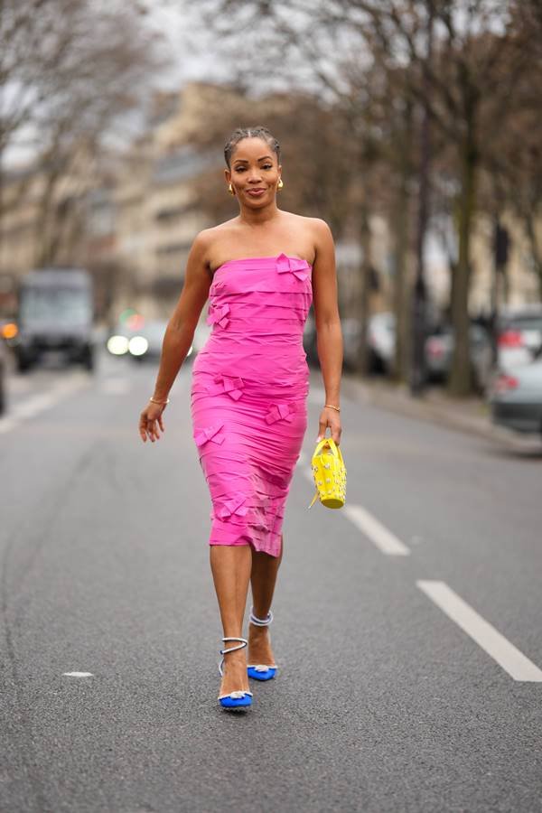 Na rua, mulher anda usando vestido rosa sem alças e segura bolsa amarela.Nos pés, sandália de salto com tiras nos tornozelos - Metrópoles